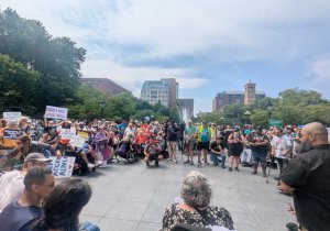 Crowd of people gathered in a park plaza for a disability rights rally holding protest signs.