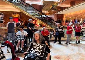 Disability rights protesters holding signs inside a building lobby near escalators.