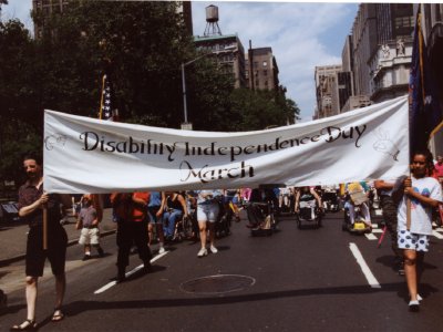 Two people holding a wide white banner as a crowd marches down a city street.