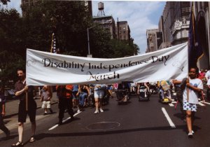 Two people holding a wide white banner as a crowd marches down a city street.