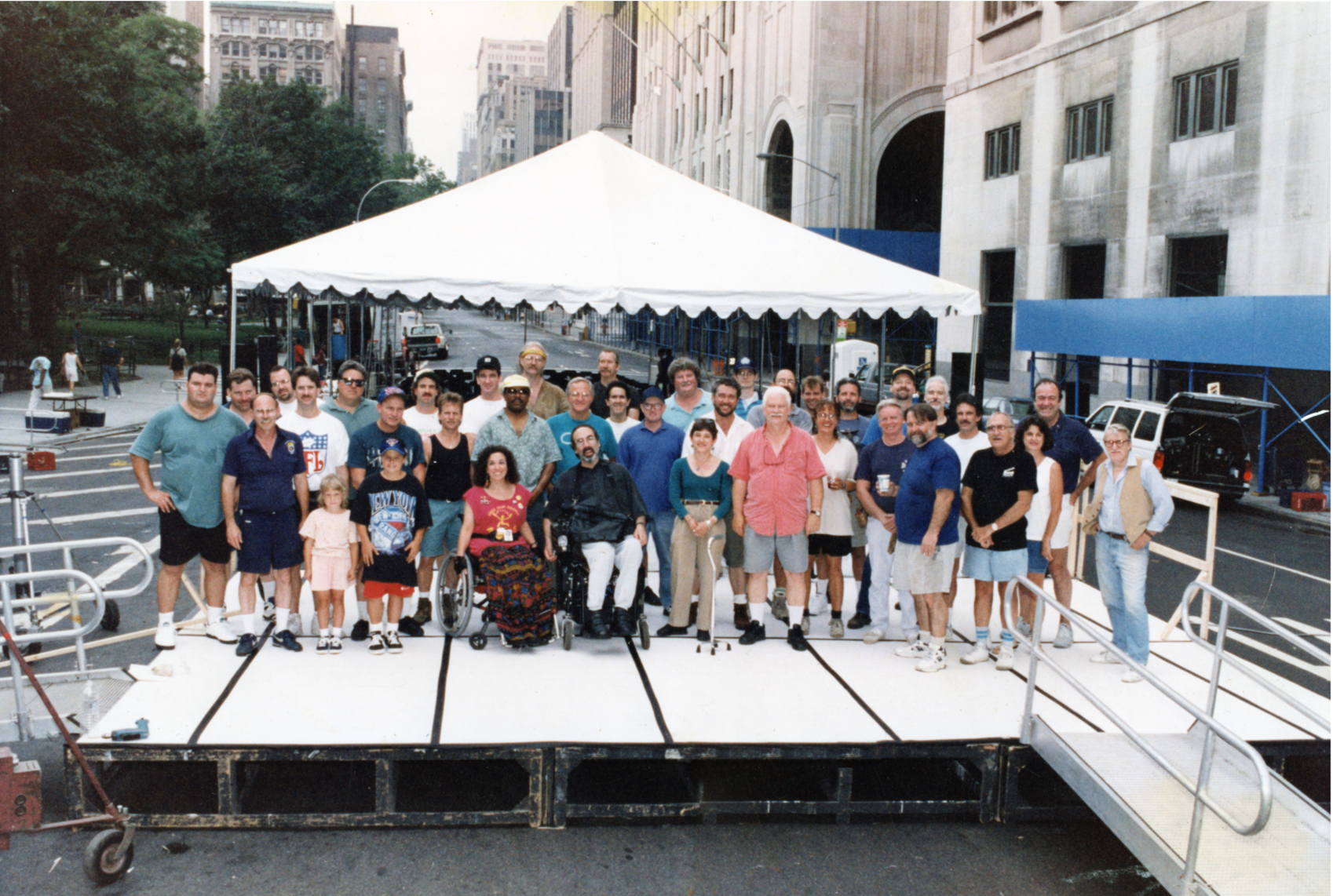 Group photo of diverse event organizers gathered on a low platform stage in a city street.