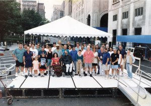 Group photo of diverse event organizers gathered on a low platform stage in a city street.
