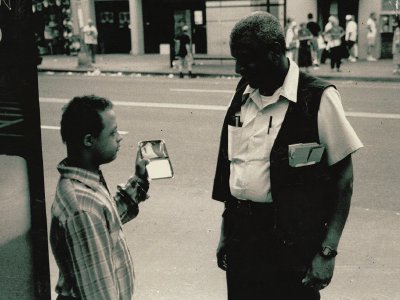 A young man asks a bus operator for directions, showing his phone