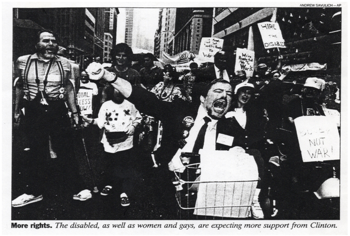 A black and white news photo of a passionate crowd of disability rights protesters shouting and raising their fists.