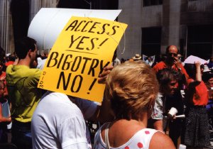 A protester in a crowd holds up a bright yellow sign, hiding their face.