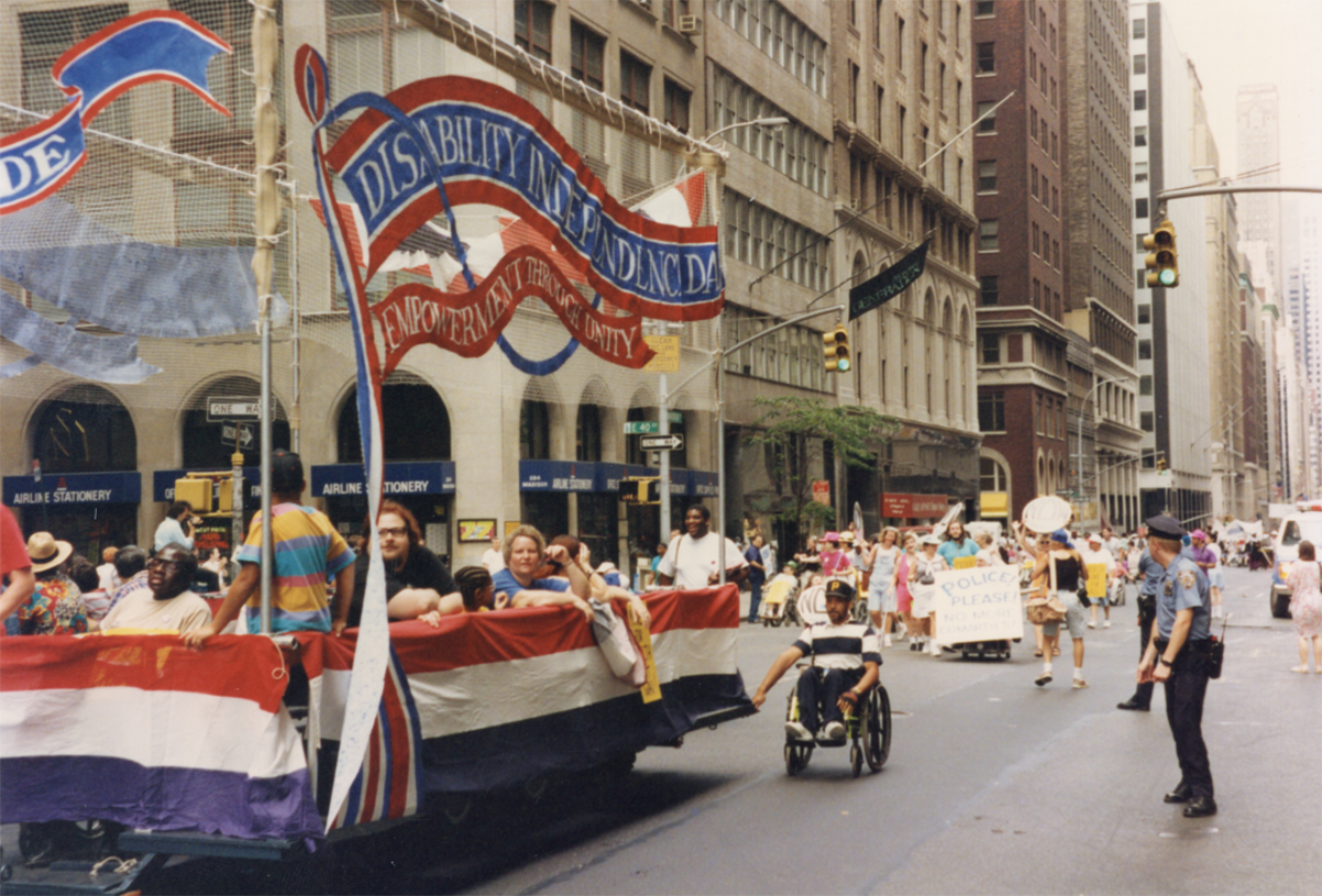 Parade float decorated with patriotic banners moving past spectators and police on a city street.