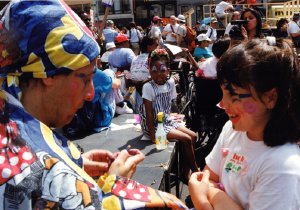 Chidren have their faces painted like clowns by an adult with clown makeup