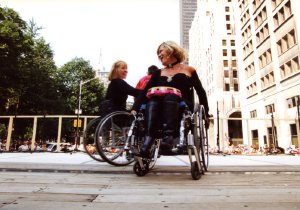 Two women in wheelchairs dance together on a wide, wooden outdoor stage during a rally.