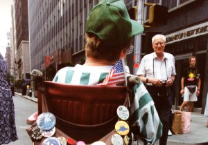 Back of a wheelchair covered in advocacy buttons, featuring an ADA badge and a small American flag.